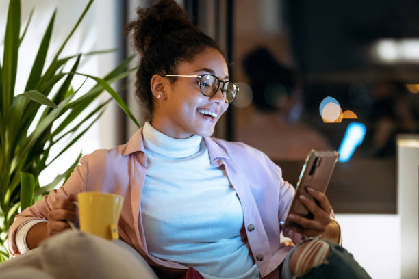 Shot of happiness young entrepreneur woman using her smart phone while drinking a cup of coffee sitting on couch in the office.